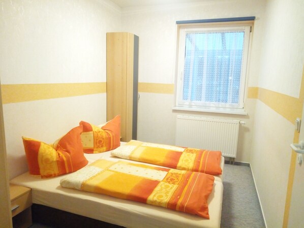 A small, single-bed room with a window, a radiator, and a wooden wardrobe.