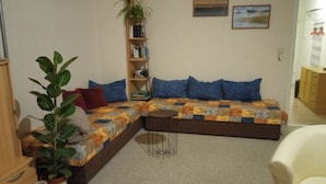 A living room with a sofa, a bookshelf, a potted plant, and a chair.