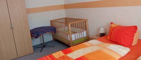 A room with a bed, a crib, a wardrobe, and a table with a tablecloth.