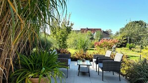 Un espacio al aire libre con mobiliario de mimbre, una mesa de vidrio y una planta en maceta.