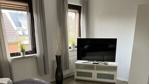 Una habitación de hotel con una cama, un televisor, un aparador y una ventana con cortinas.