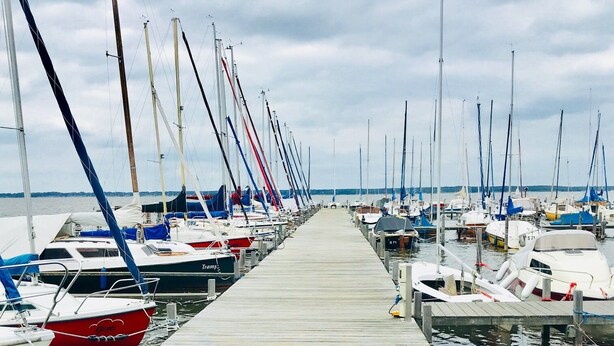 Un muelle de madera que lleva a un puerto deportivo con varias embarcaciones amarradas a ambos lados.