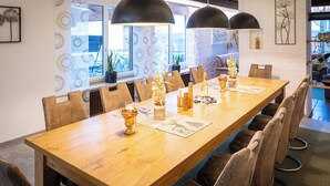 Una larga mesa de madera para comer con sillas, dos lámparas colgantes y elementos decorativos.