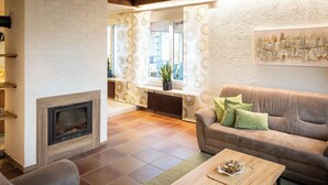 Una sala de estar con chimenea, un sofá, una mesa de centro y vista a la cocina a través de una puerta de vidrio.