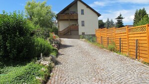 A two-story building with a balcony, a cobblestone path leading to the entrance, and a wooden fence on the right. - Experience nature - enjoy peace (Mohlsdorf-Teichwolframsdorf)