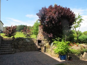 A stone building with a chimney, surrounded by a garden with various plants and a brick pathway.