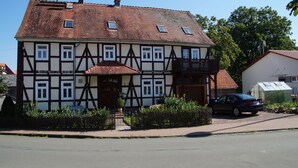 Ein traditionelles Fachwerkhäuschen mit geneigtem Dach und einem kleinen Balkon, vor dem ein Auto geparkt ist.