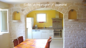 Uma área de refeições com um arco de pedra, parede amarela e cozinha ao fundo.