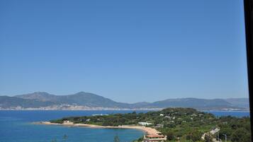 A coastal landscape with a beach, buildings, and mountains in the background.