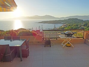 Een terras met een tafel, stoelen, een barbecue en uitzicht op zee en bergen.