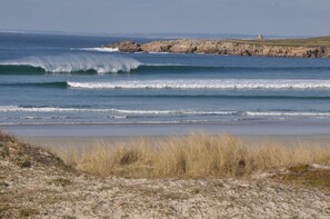 A coastal beach with waves, a rocky outcrop, and a grassy area. - Penmarc’h-Holiday Cottage (Penmarch)