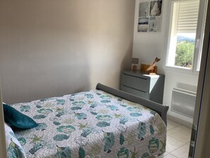 Une chambre à coucher comprenant un lit, une table de chevet, une commode et une fenêtre donnant sur un paysage verdoyant.