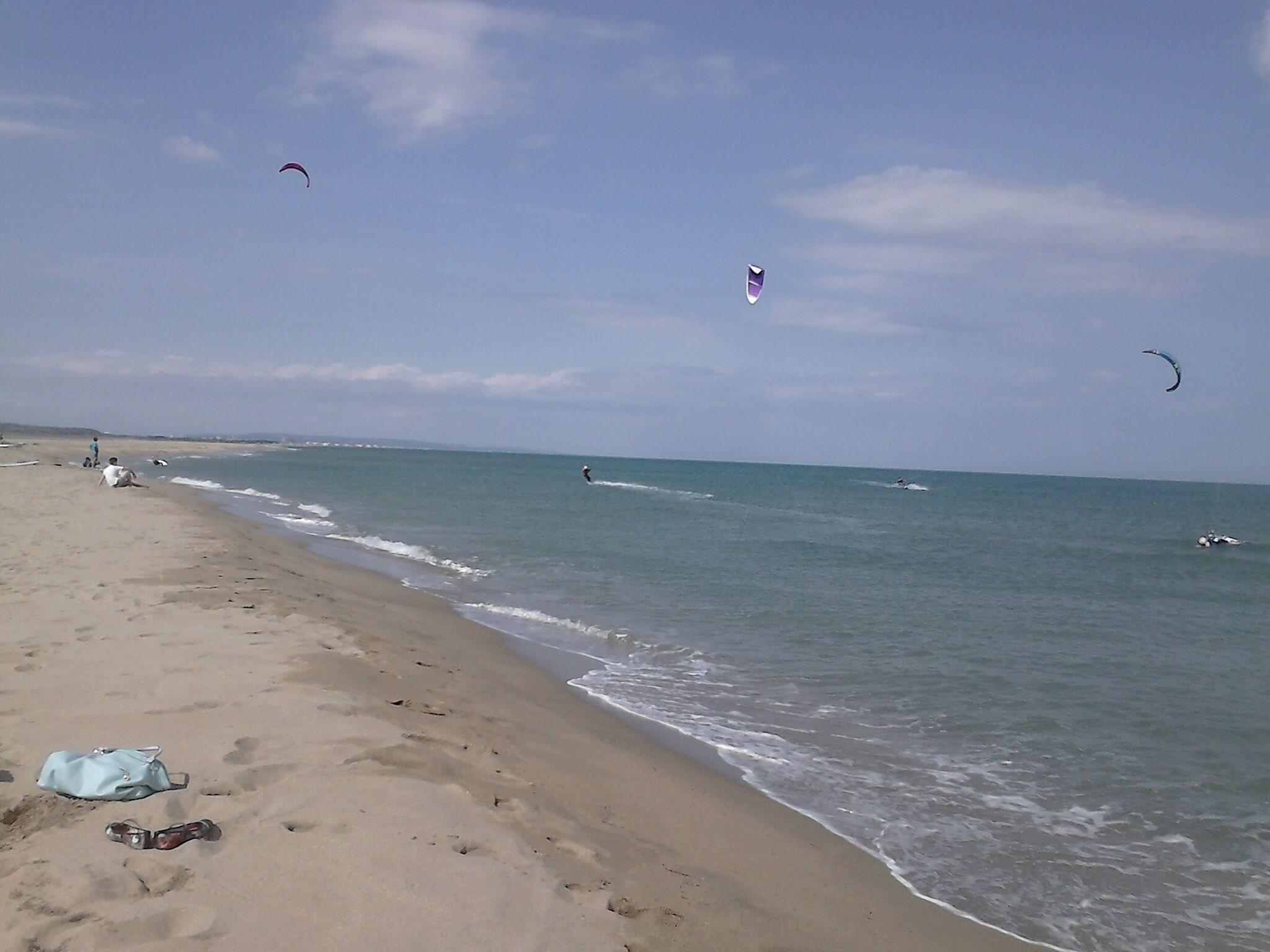 Une plage avec un ciel dégagé, une mer calme et des gens qui pratiquent des activités nautiques.