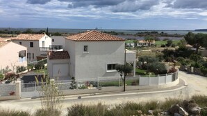 A residential area with houses, a paved road, and a body of water in the background. - VILLA AND GARDEN in the SOLEIL  (La Palme)