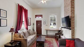 A living room with a sofa, armchair, coffee table, and a TV mounted on a brick wall.