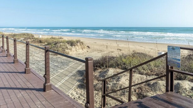 Pasarela de madera que conduce a una playa, con un letrero que indica que no hay socorrista de servicio.