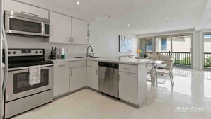 Una cocina moderna con electrodomésticos de acero inoxidable, lavavajillas y comedor con vistas al balcón.