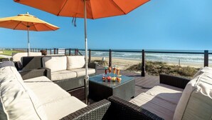 Un patio con mobiliario de mimbre y una sombrilla naranja, con vista a la playa.