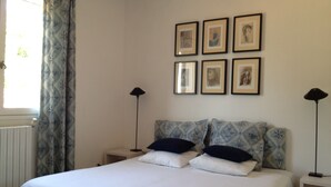 Ein Schlafzimmer mit einem Bett, zwei Nachttischen, einem Fenster mit Vorhängen und sechs gerahmten Bildern an der Wand.
