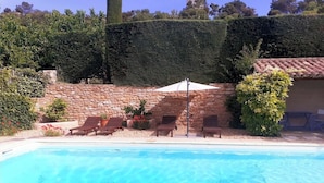 Ein Schwimmbecken mit Liegestühlen und Sonnenschirm, umgeben von Steinmauern und Grünpflanzen.