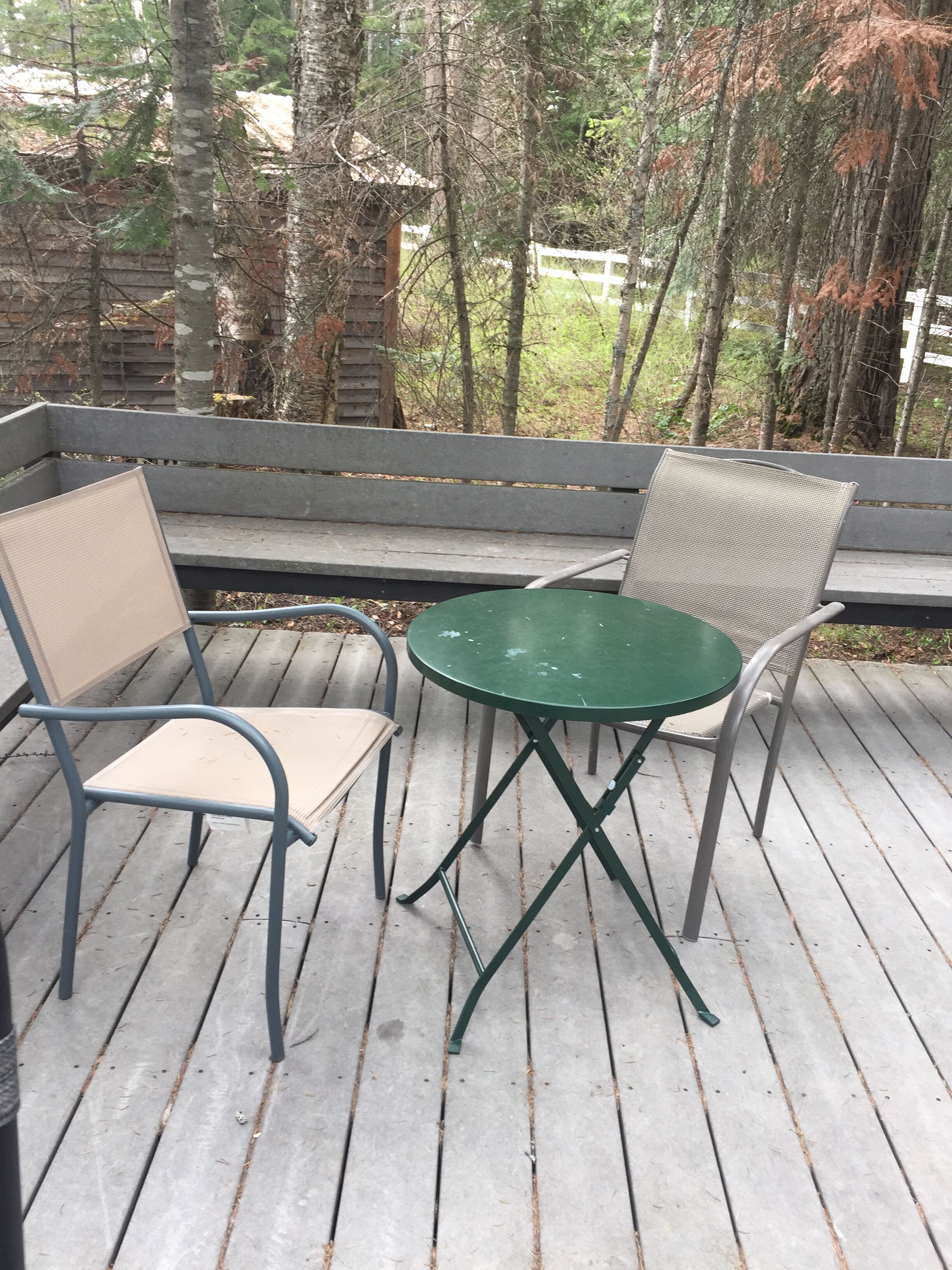 A wooden deck with a green table and two chairs.