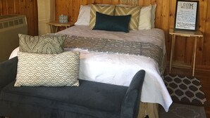 Ein Zimmer mit Holzwandverkleidung, einem Bett, einer Bank, einem Schild und einem Gemälde.