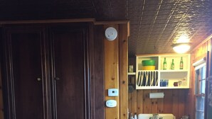 Ein Zimmer mit einem großen Holzschrank, einer kleinen Küchenzeile inklusive Spüle und Schränken sowie einem blauen Stuhl.