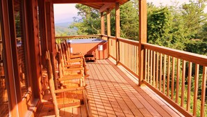 Um deck de madeira com área de estar externa e hidromassagem, com vista para uma área arborizada.
