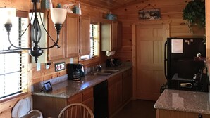 Cozinha de cabana de madeira com mesa e cadeiras de madeira, cafeteira e frigorífico.