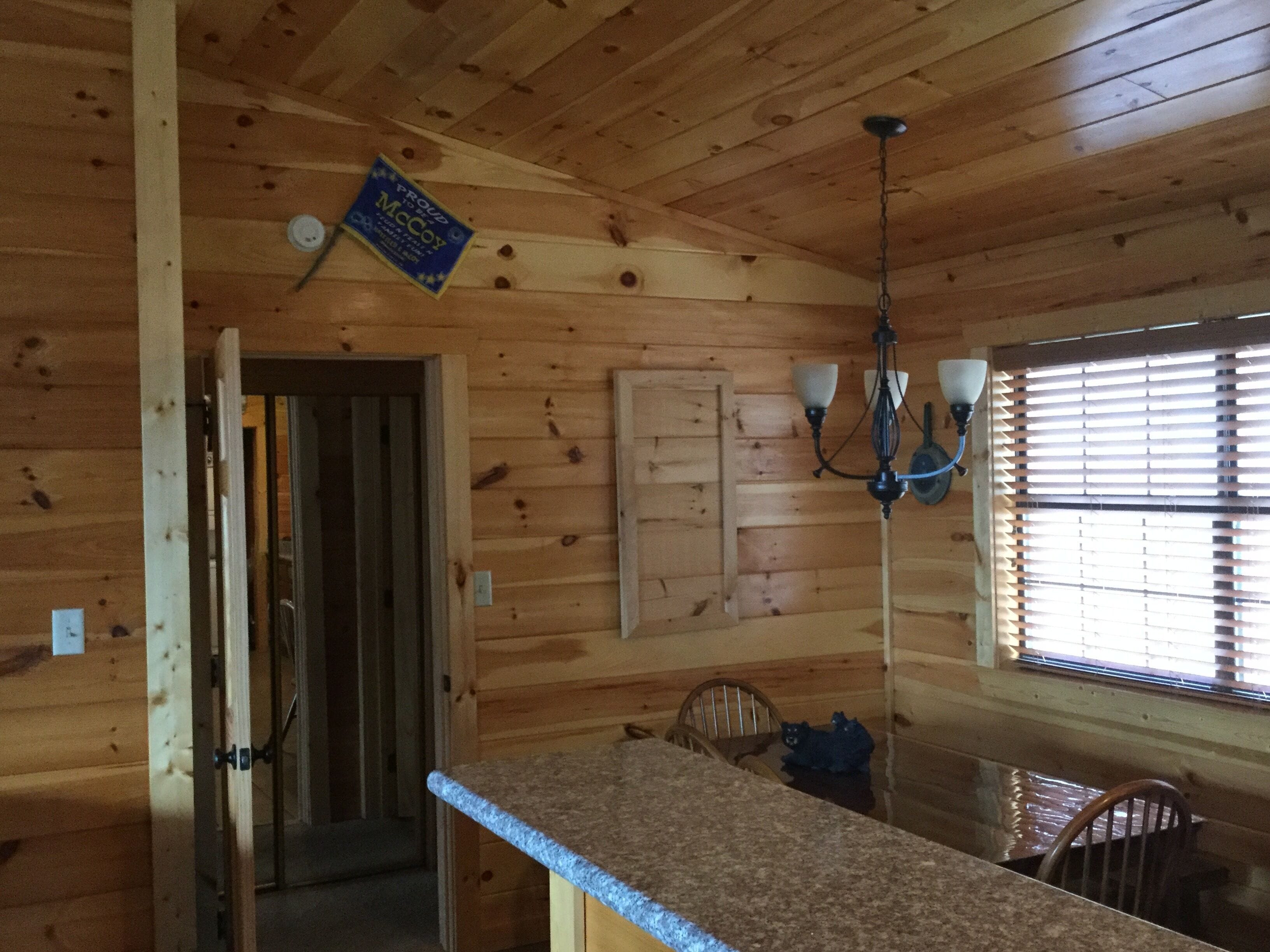 A wooden cabin interior with a kitchen area, a dining table, and a chandelier.