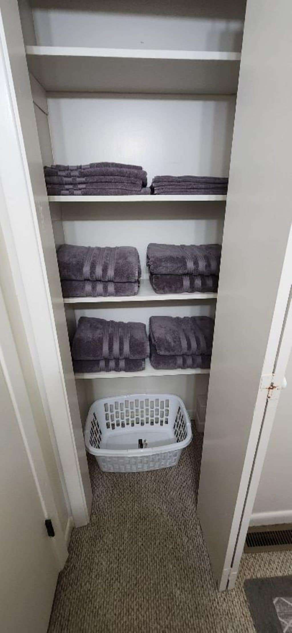 Un armario con estantes que contienen toallas dobladas y un cesto de ropa en el suelo.