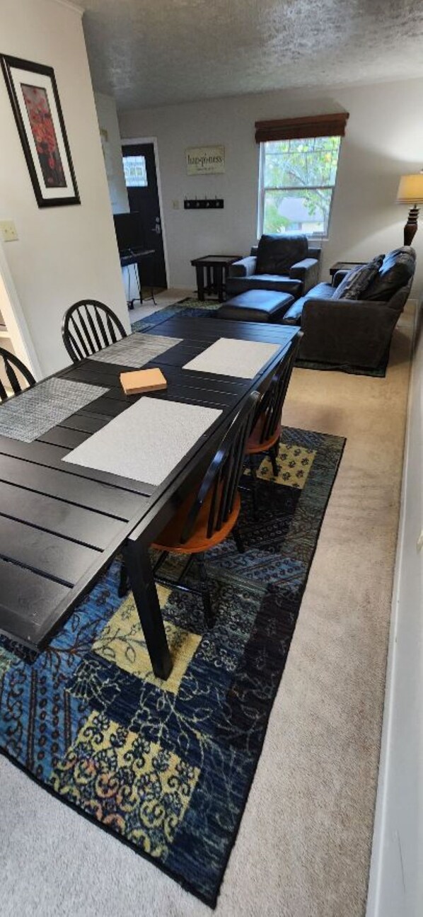 Un espace repas avec une longue table, des chaises noires et un tapis à motifs.