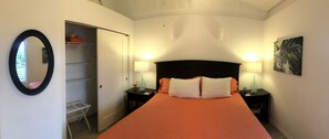 Habitación de hotel con cama, dos lámparas de noche, mesita de noche, espejo, armario y un cuadro en la pared.