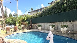 A swimming pool with a white inflatable unicorn float, surrounded by lounge chairs and potted plants.