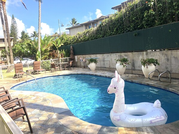 Una piscina con un flotador hinchable de unicornio blanco, rodeada de sillas de descanso y plantas en macetas.