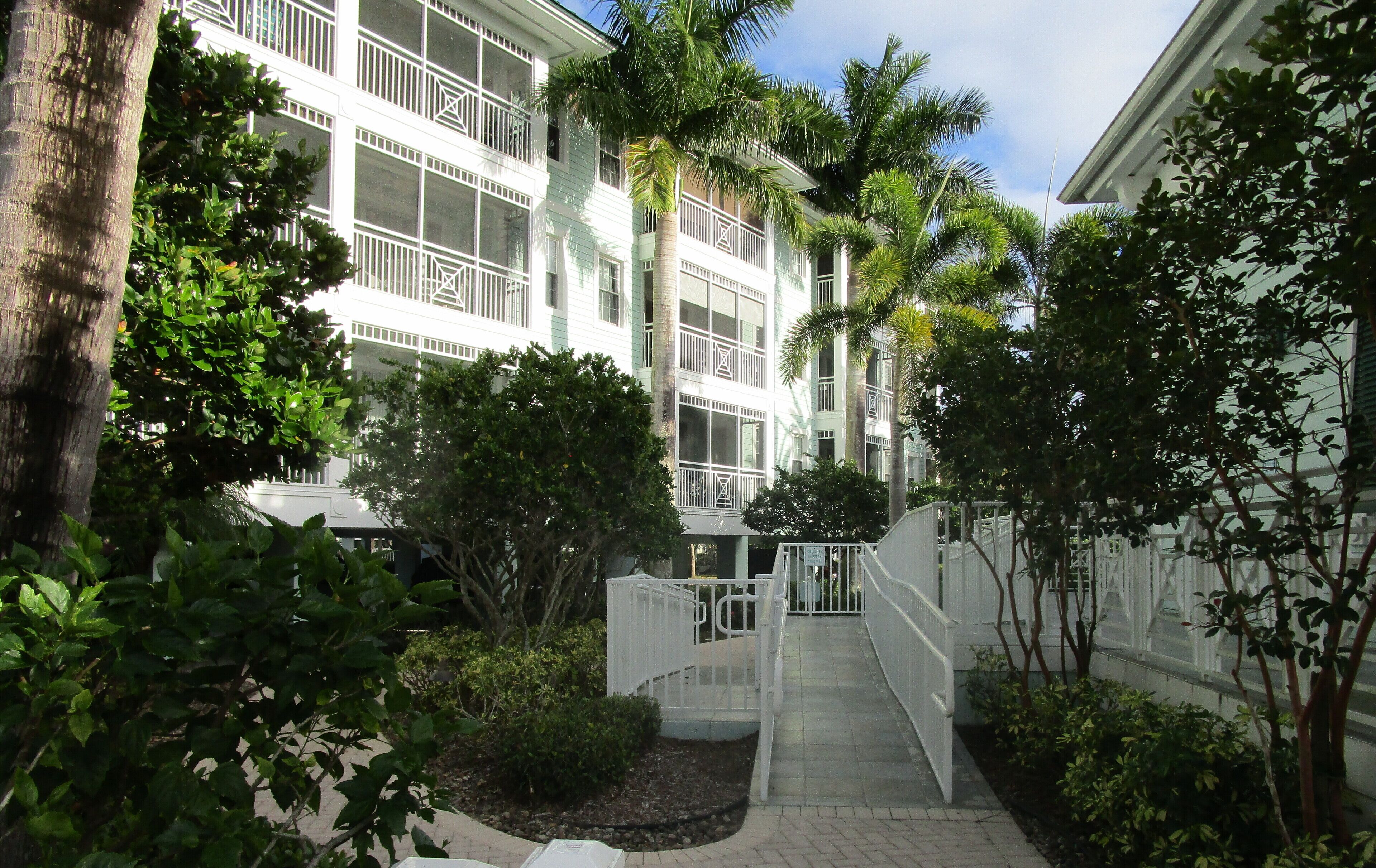 A multi-story hotel with balconies, surrounded by lush greenery and a paved walkway.