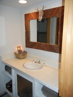 Ein Badezimmer mit einem weißen Waschbecken, einem Spiegel mit Holzrahmen und einem dekorativen Hirschkopf darüber.
