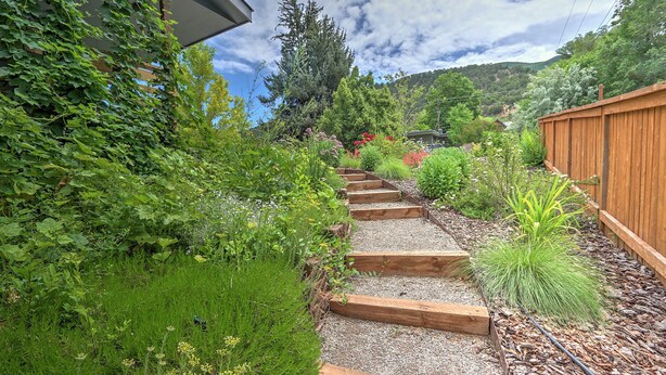 A garden pathway with wooden steps leading to a house surrounded by lush greenery and a wooden fence. - Mid Century Home with a Modern Twist in Downtown. Proximate to Everything w/AC! (Glenwood Springs)