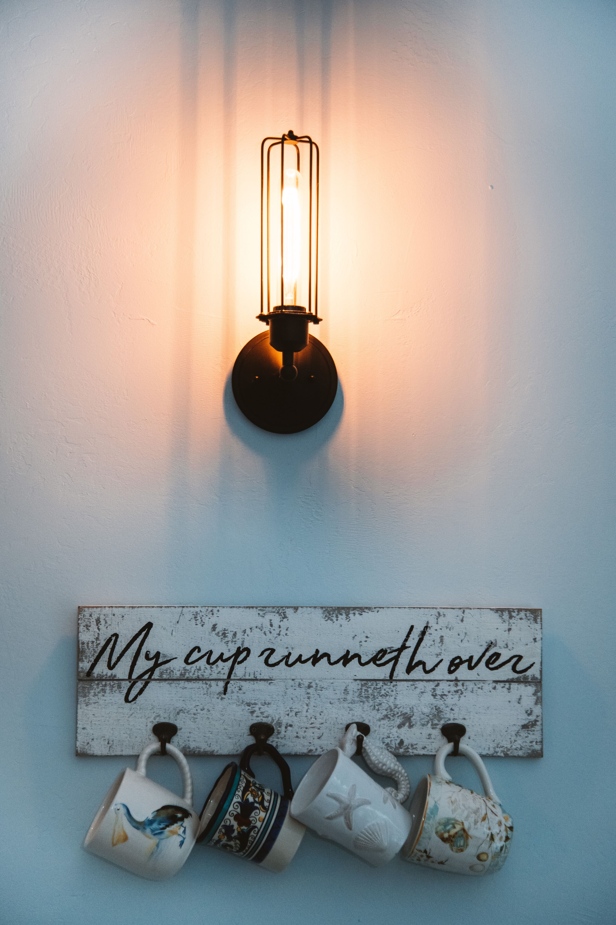 Uma luminária fixada na parede, com uma placa abaixo que diz 'My cup runneth over'.