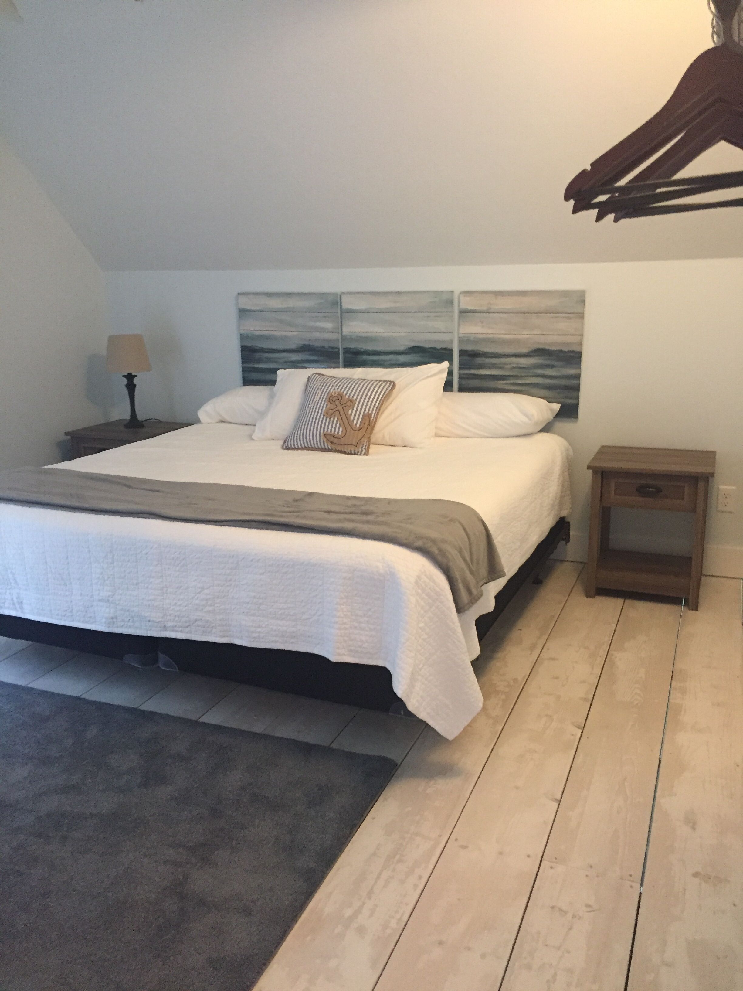 A bedroom with a bed, a nightstand, a lamp, a painting on the wall, and a wooden floor.