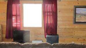 Ein Holzblock-Innenraum mit einer Ledersitzgruppe, einem Fernseher und einem Fenster mit roten Vorhängen.