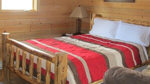 Ein Schlafzimmer einer Holzhütte mit einem Bett, einem Nachttisch, einer Lampe und einem Fenster.