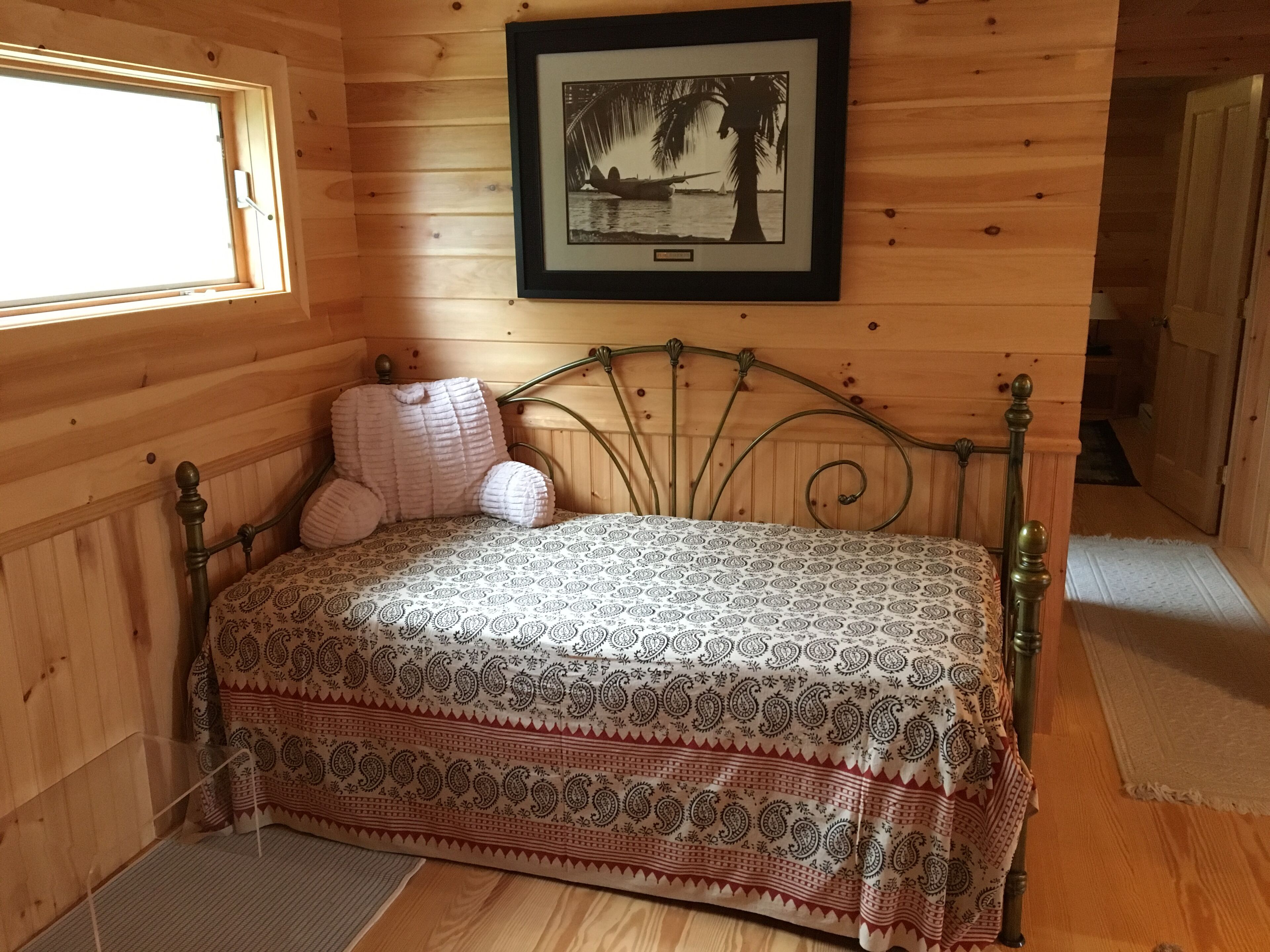 Ein Schlafzimmer einer Holzhütte mit einem Bett, einem gerahmten Bild an der Wand und einem Fenster.