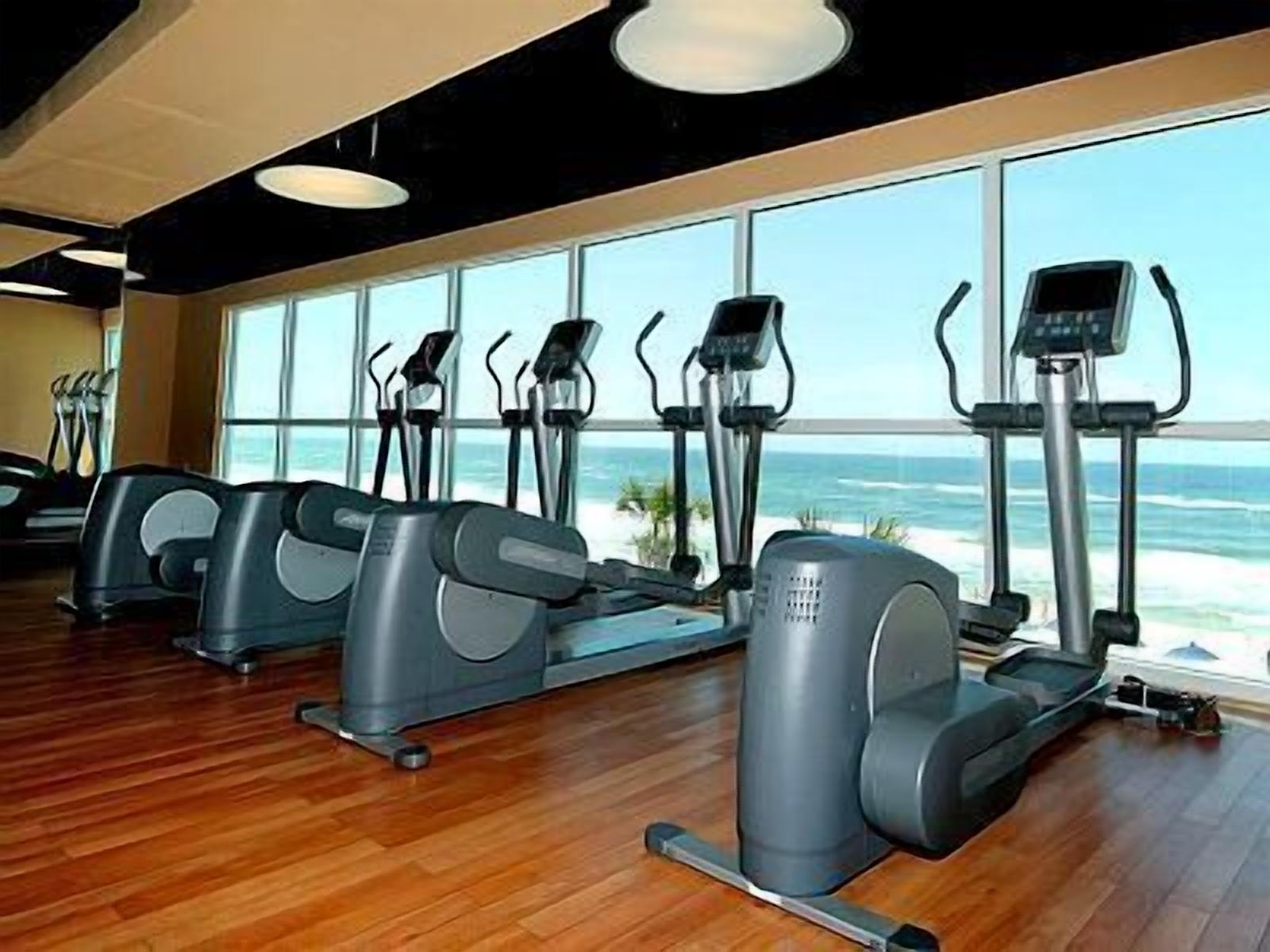 A gym with cardio machines and large windows overlooking the ocean.