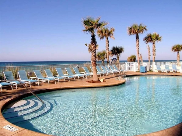 Relax by the ocean-view pool surrounded by palm trees and lounge chairs.