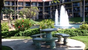 A hotel courtyard with a fountain, palm trees, and a pool. - OCEAN VIEW, LARGE LANAI, STEPS FROM THE BEACH, BLDG 10 (Kihei)