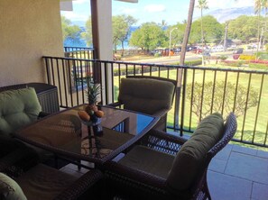 A balcony with wicker furniture, a glass table, and a view of a park and road.