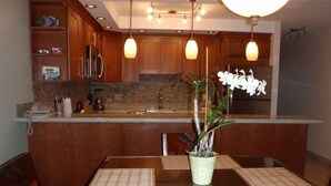 A modern kitchen with wooden cabinets, a granite countertop, and pendant lighting. - OCEAN VIEW, LARGE LANAI, STEPS FROM THE BEACH, BLDG 10 (Kihei)