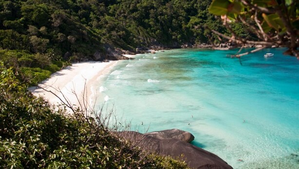 Una playa con agua turquesa cristalina, arena blanca y colinas verdes exuberantes al fondo.