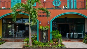 Un edificio de fachada roja, puertas turquesas y un pequeño jardín con una palmera.